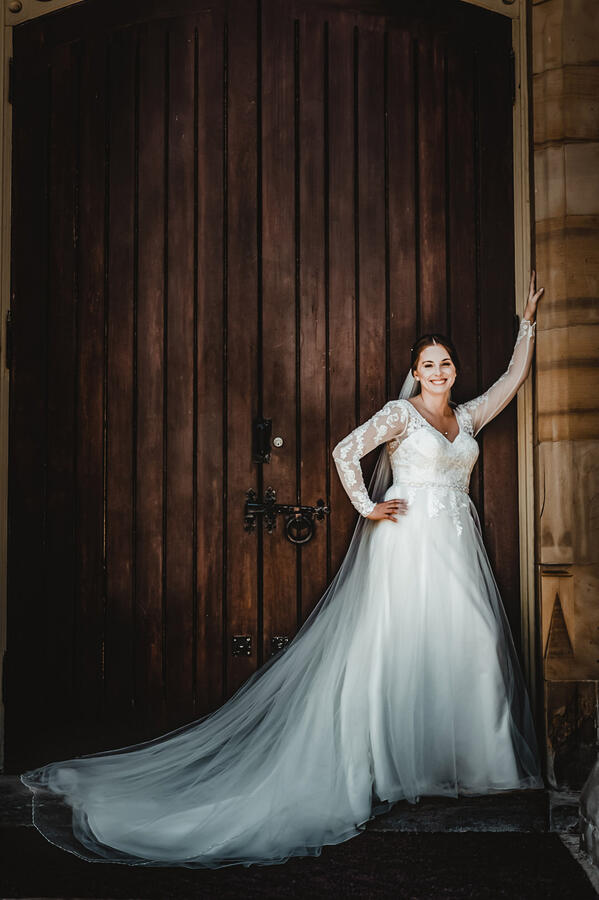 Untitled Bride with arm up against an old doorframe, smiling at camera