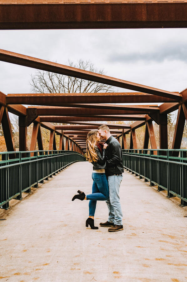 Untitled Couple - standing on a bridge, snuggling up to one another, with a foot pop